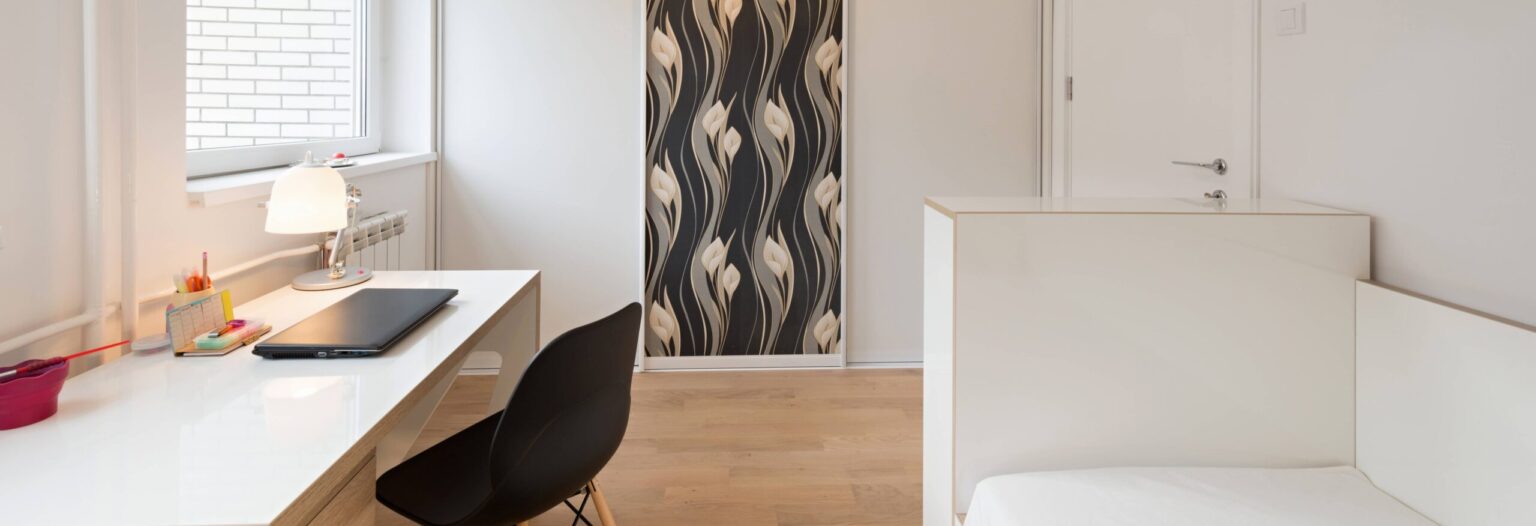 Studio étudiant meublé et lumineux avec bureau blanc, chaise design noire et lit, idéal pour un investissement locatif