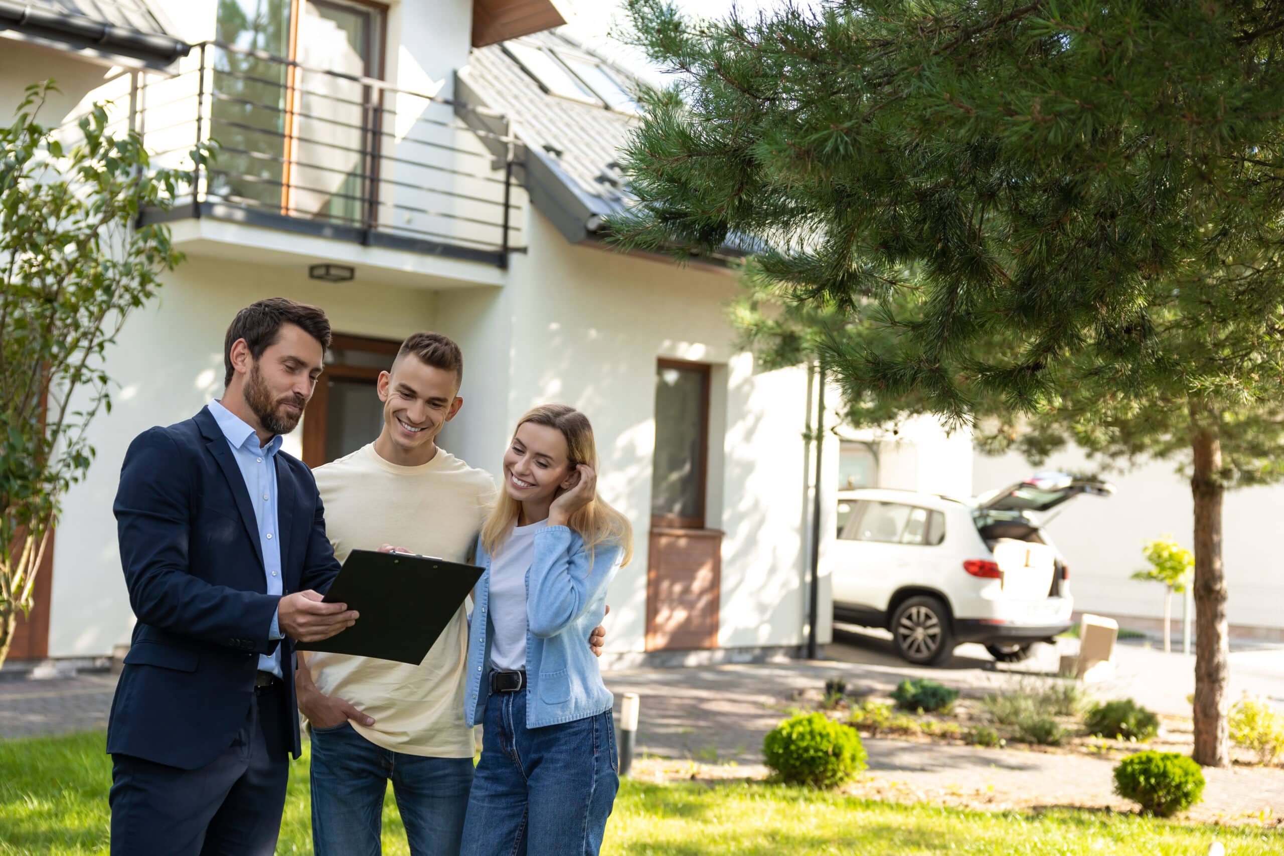 Un agent immobilier présente un porte-documents à un couple devant une propriété résidentielle.
