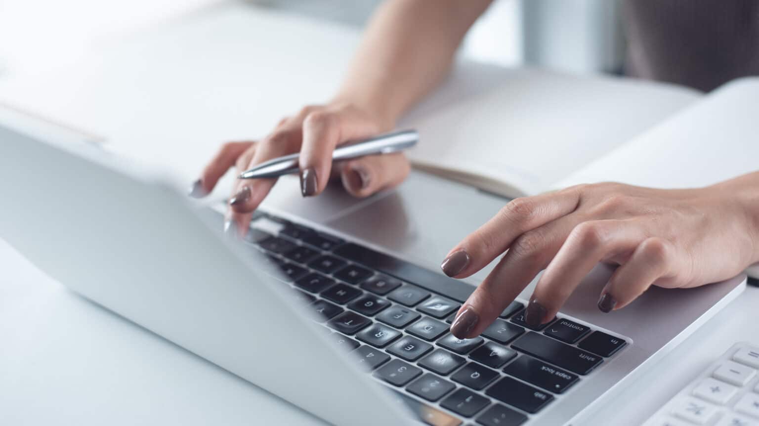 Gros plan sur la main d'une femme tapant sur un ordinateur portable posé sur son bureau, effectuant des recherches en ligne.