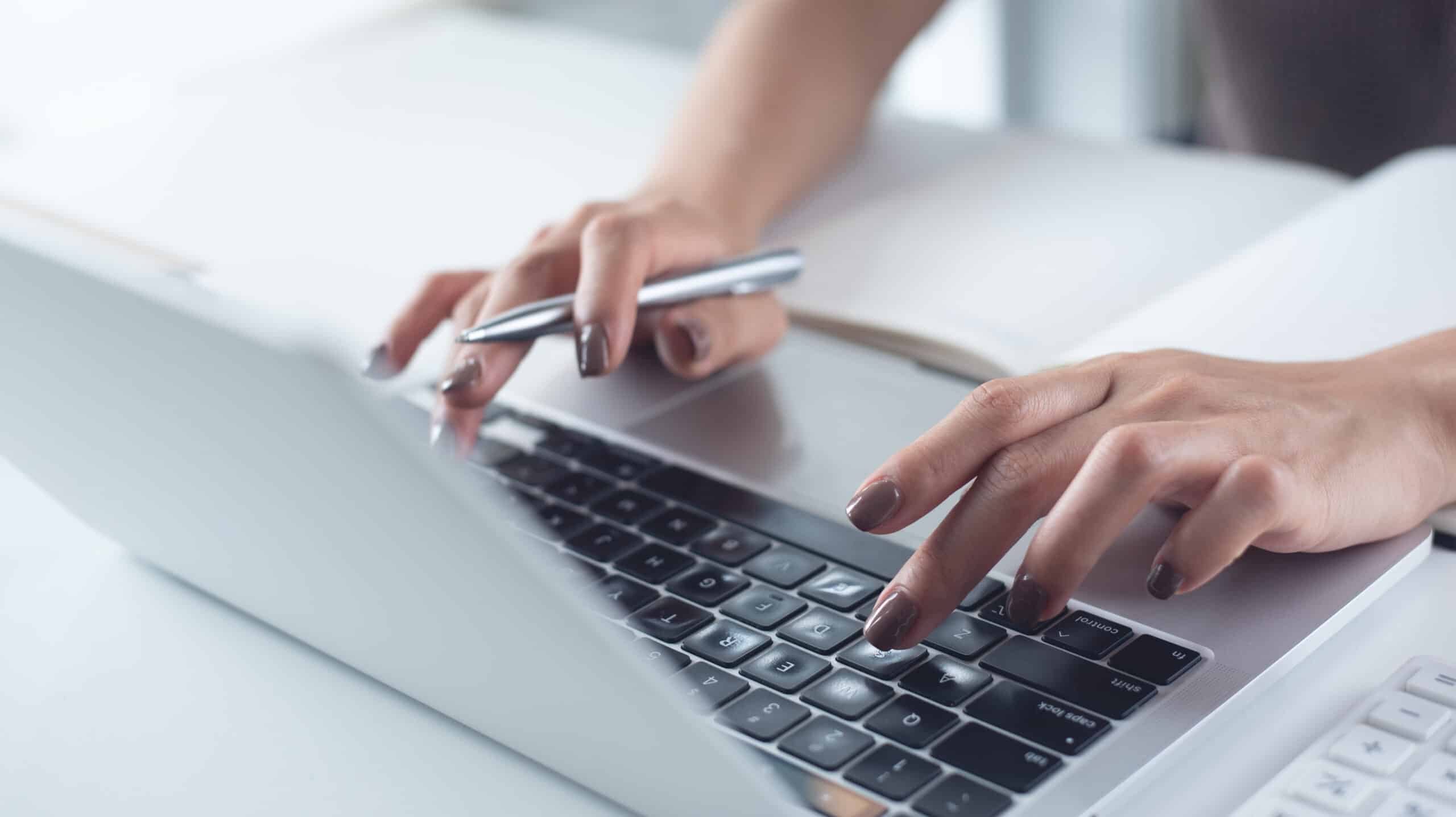 Gros plan sur la main d'une femme tapant sur un ordinateur portable posé sur son bureau, effectuant des recherches en ligne.