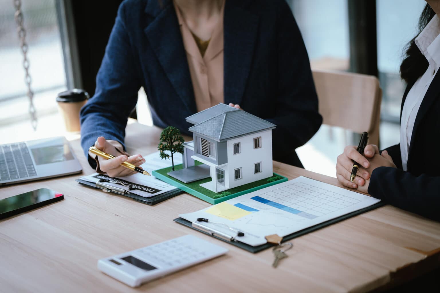 Des professionnels du secteur immobilier discutent d'un modèle de maison, documents et calculatrice à l'appui, dans le cadre de leurs activités de planification immobilière, d'investissement immobilier et de conseil en achat de maison.