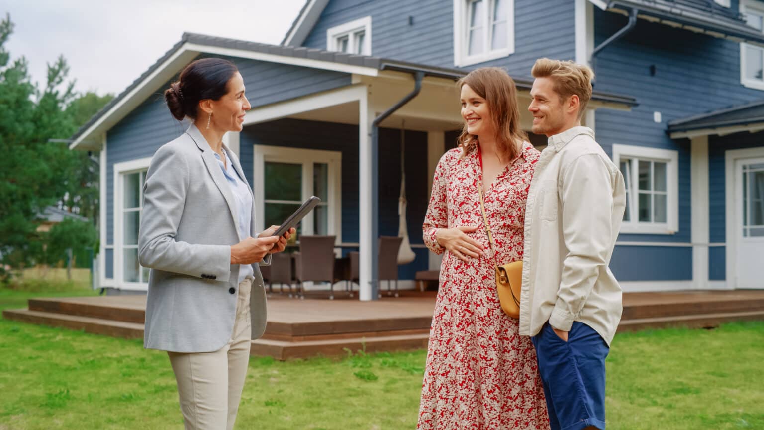 Un jeune couple visite une maison potentielle en compagnie d'un agent immobilier. L'agent, une femme, fait visiter la maison aux futurs propriétaires. Gros plan sur le panneau « À vendre ».