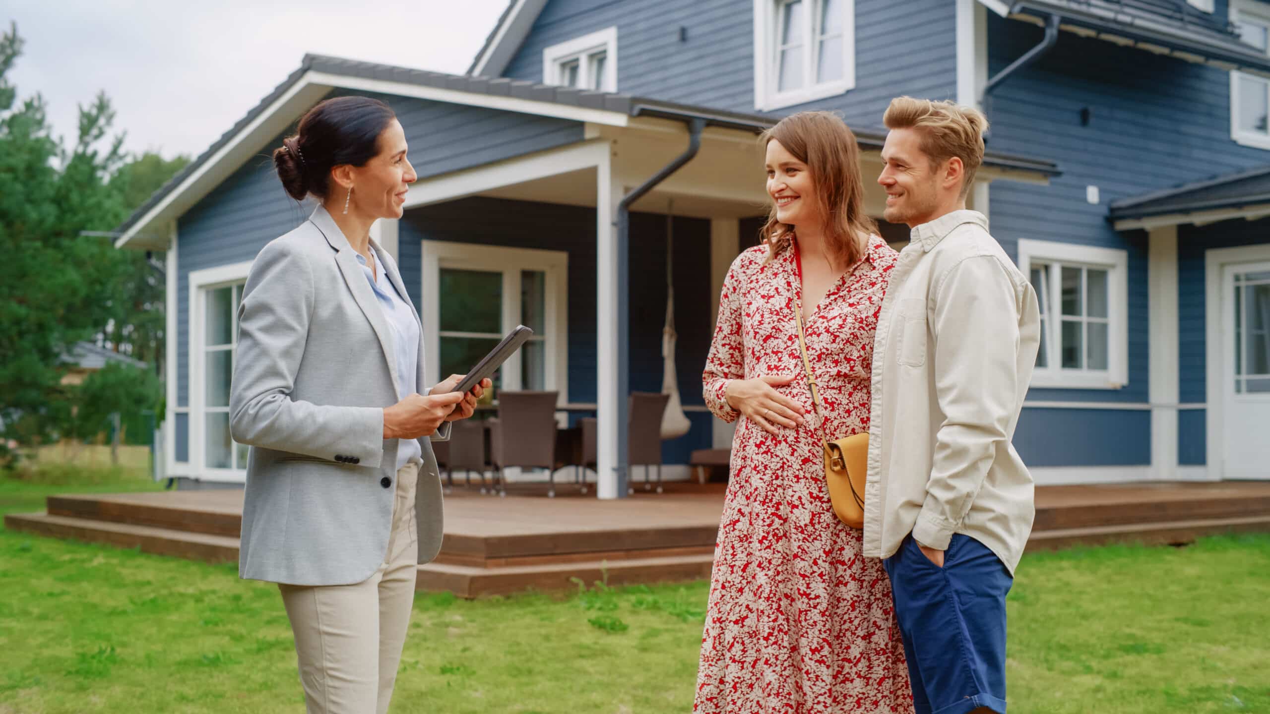 Un jeune couple visite une maison potentielle en compagnie d'un agent immobilier. L'agent, une femme, fait visiter la maison aux futurs propriétaires. Gros plan sur le panneau « À vendre ».