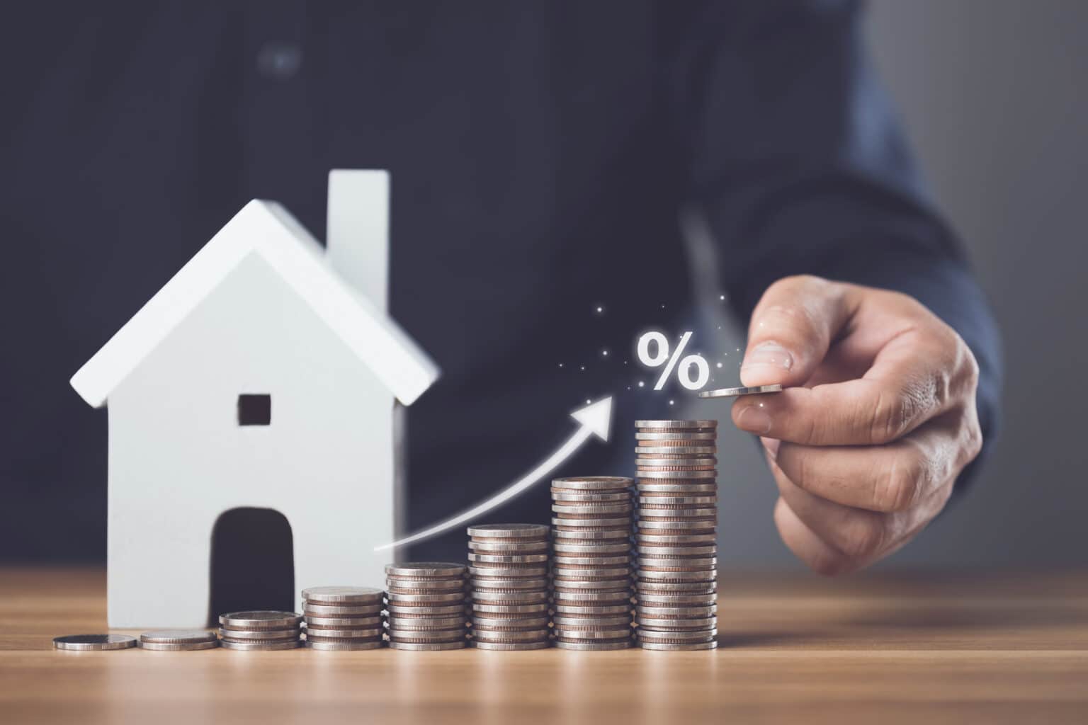 Intérêts immobiliers, taux d'intérêt pour le logement, solutions financières et commerciales pour la résidence, concept d'épargne pour le logement. Un homme empile des pièces de monnaie et une maquette de maison sur une table en bois.