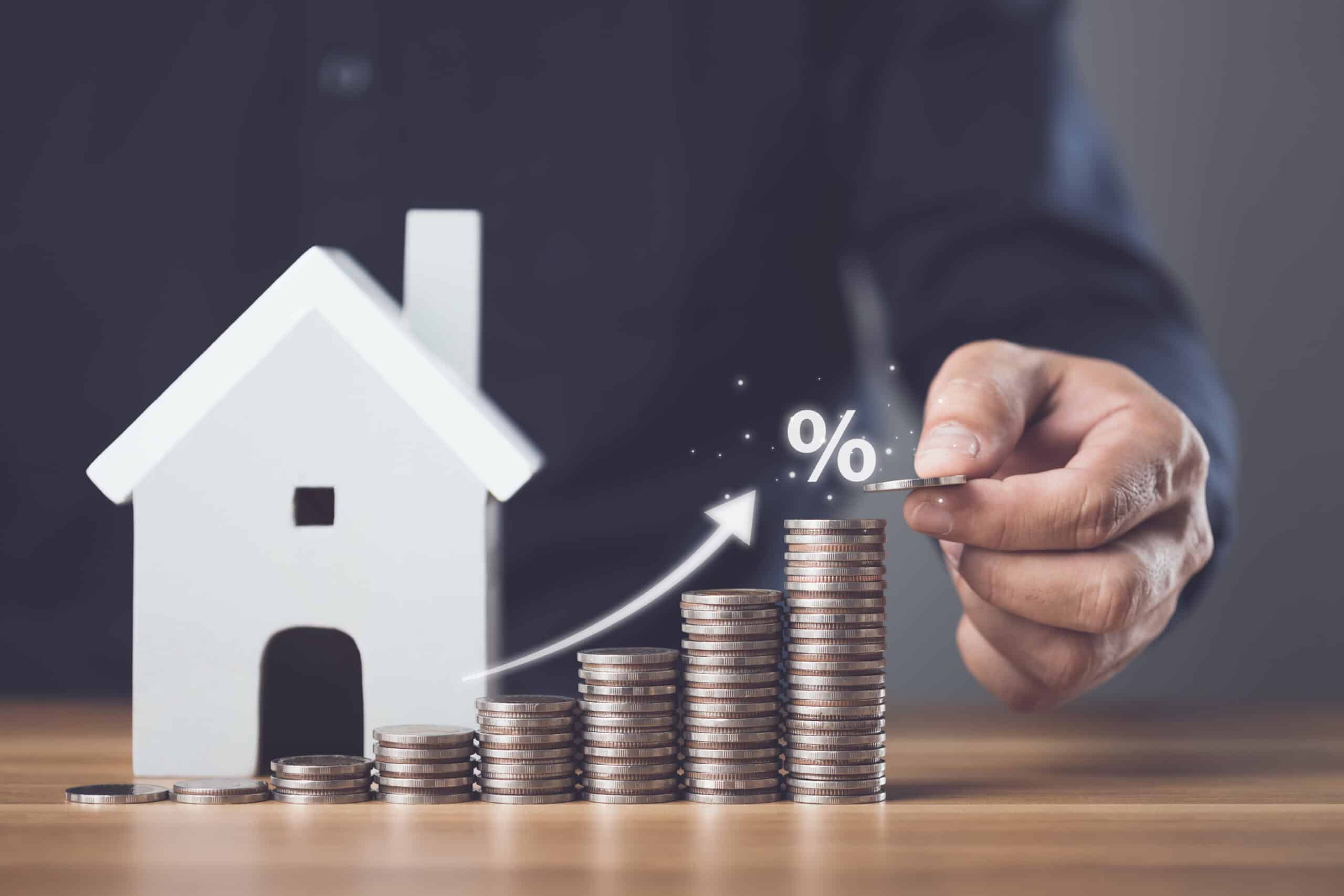 Intérêts immobiliers, taux d'intérêt pour le logement, solutions financières et commerciales pour la résidence, concept d'épargne pour le logement. Un homme empile des pièces de monnaie et une maquette de maison sur une table en bois.