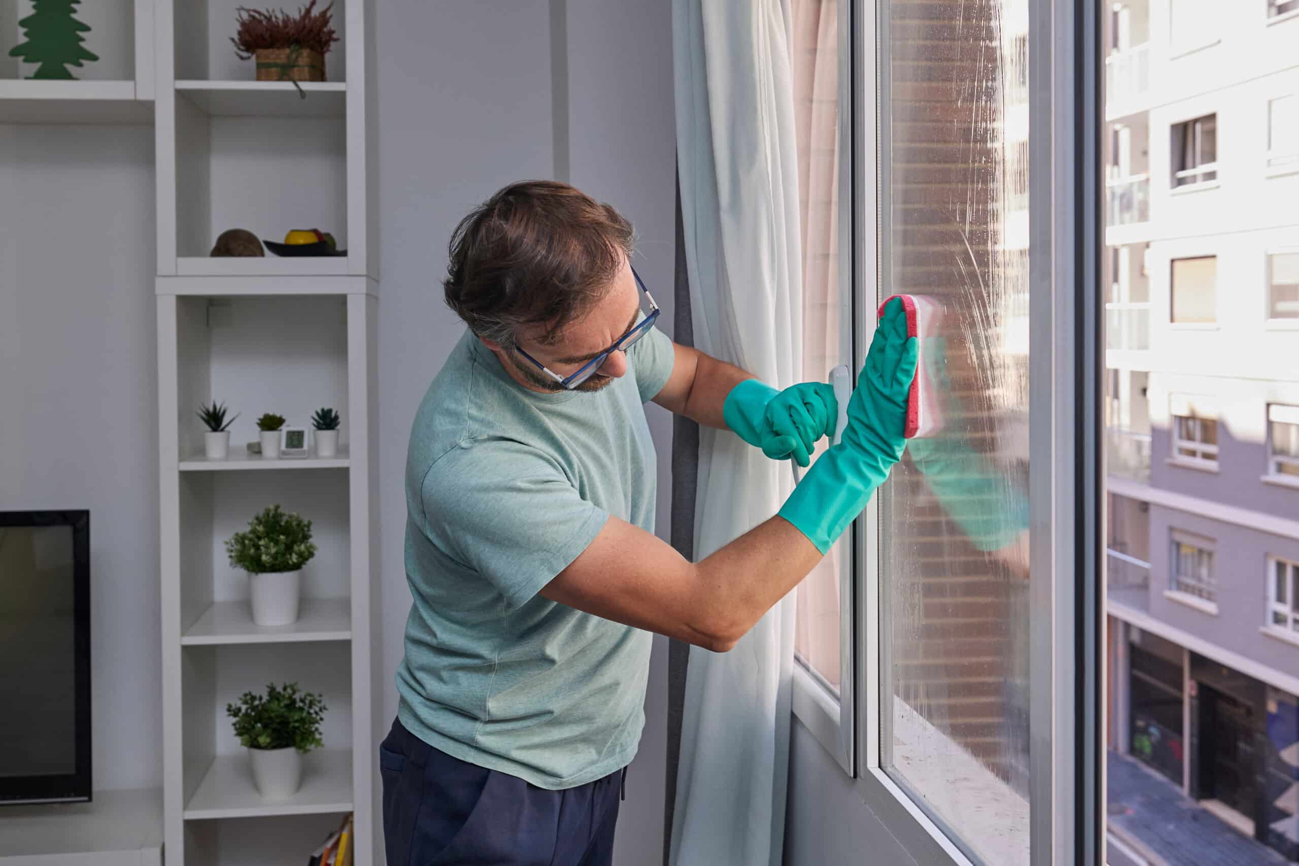 Un homme nettoie les vitres chez lui à l'aide d'une éponge et d'un vaporisateur.
