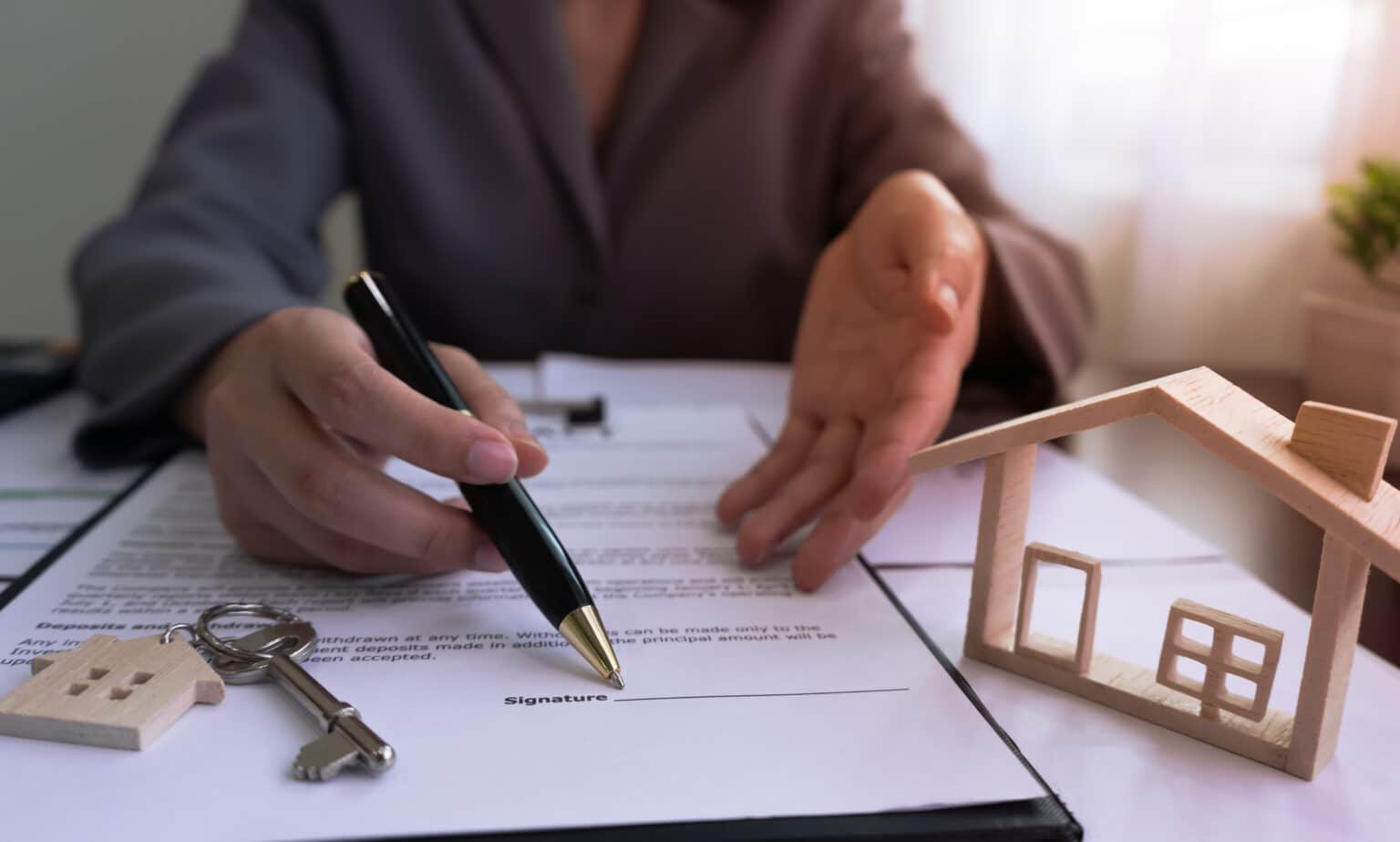 Un agent immobilier montre du doigt le panneau sur le contrat de vente de la maison, avec la maison témoin et les clés, après avoir conclu un accord avec le client.