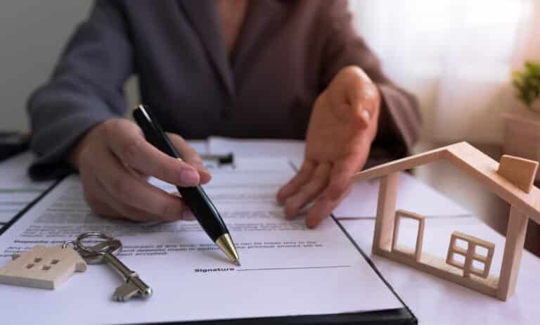Un agent immobilier montre du doigt le panneau sur le contrat de vente de la maison, avec la maison témoin et les clés, après avoir conclu un accord avec le client.