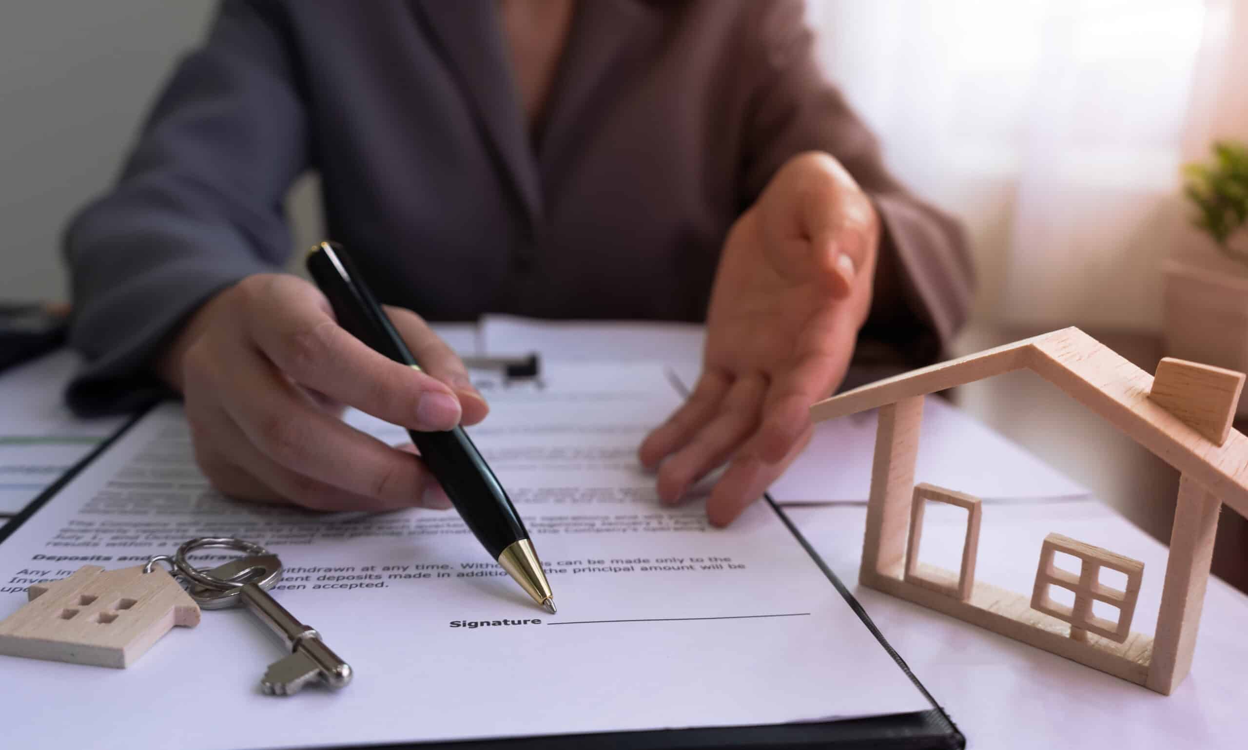 Un agent immobilier montre du doigt le panneau sur le contrat de vente de la maison, avec la maison témoin et les clés, après avoir conclu un accord avec le client.