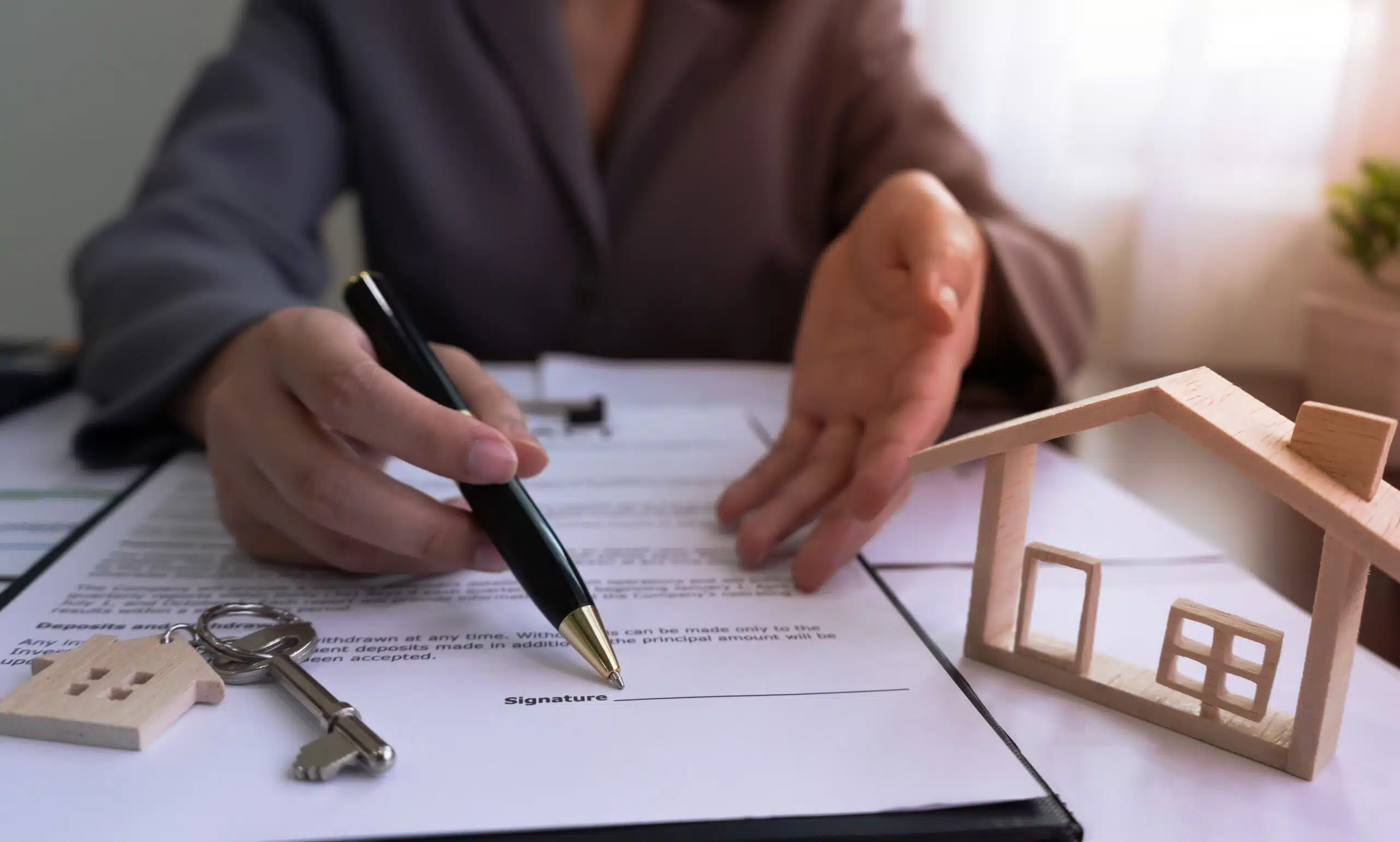 Un agent immobilier montre du doigt le panneau sur le contrat de vente de la maison, avec la maison témoin et les clés, après avoir conclu un accord avec le client.